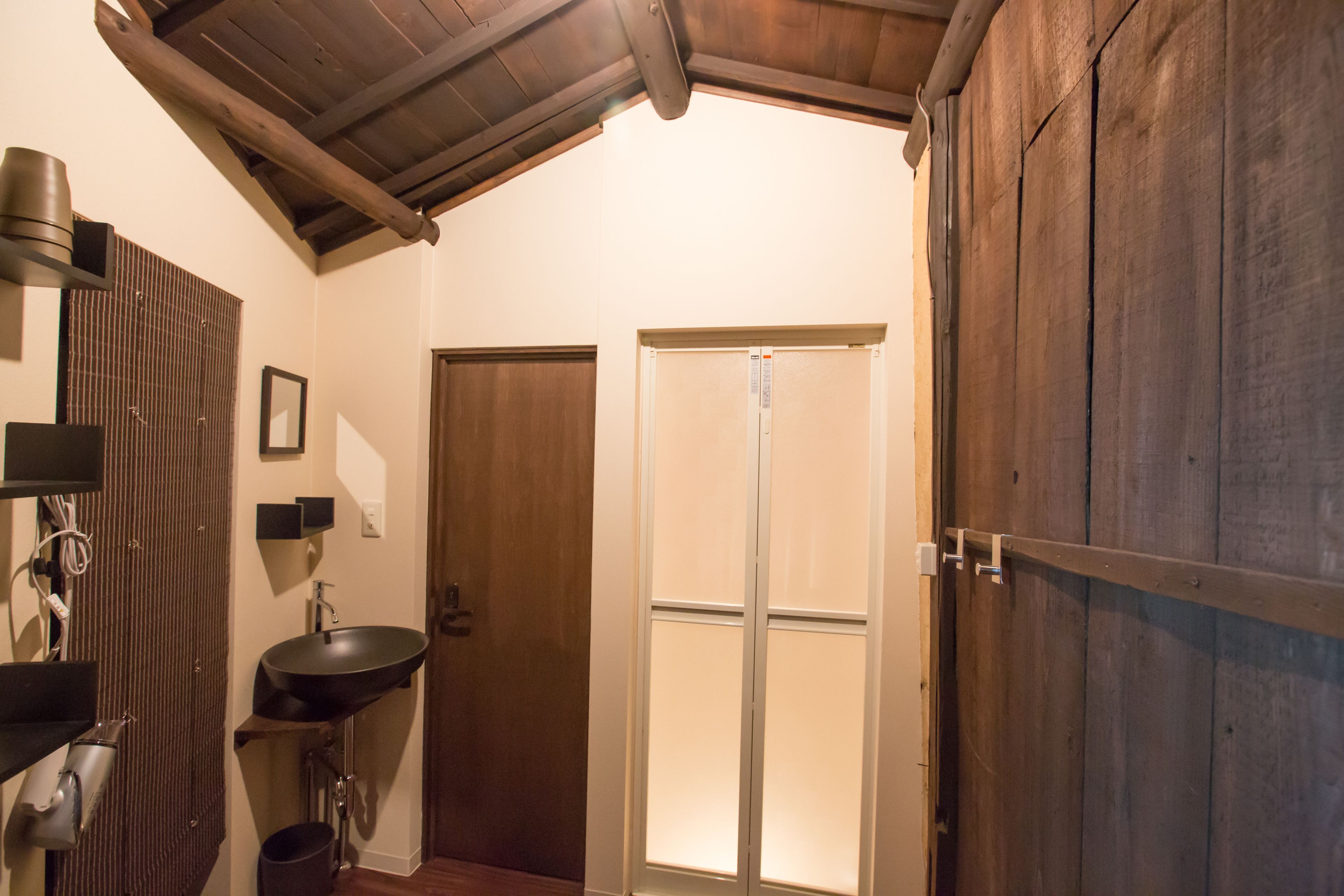 A bathroom with a wooden ceiling, a sink, a mirror, and a door leading to a shower.