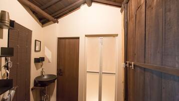 A bathroom with a wooden ceiling, a sink, a mirror, and a door leading to a shower.