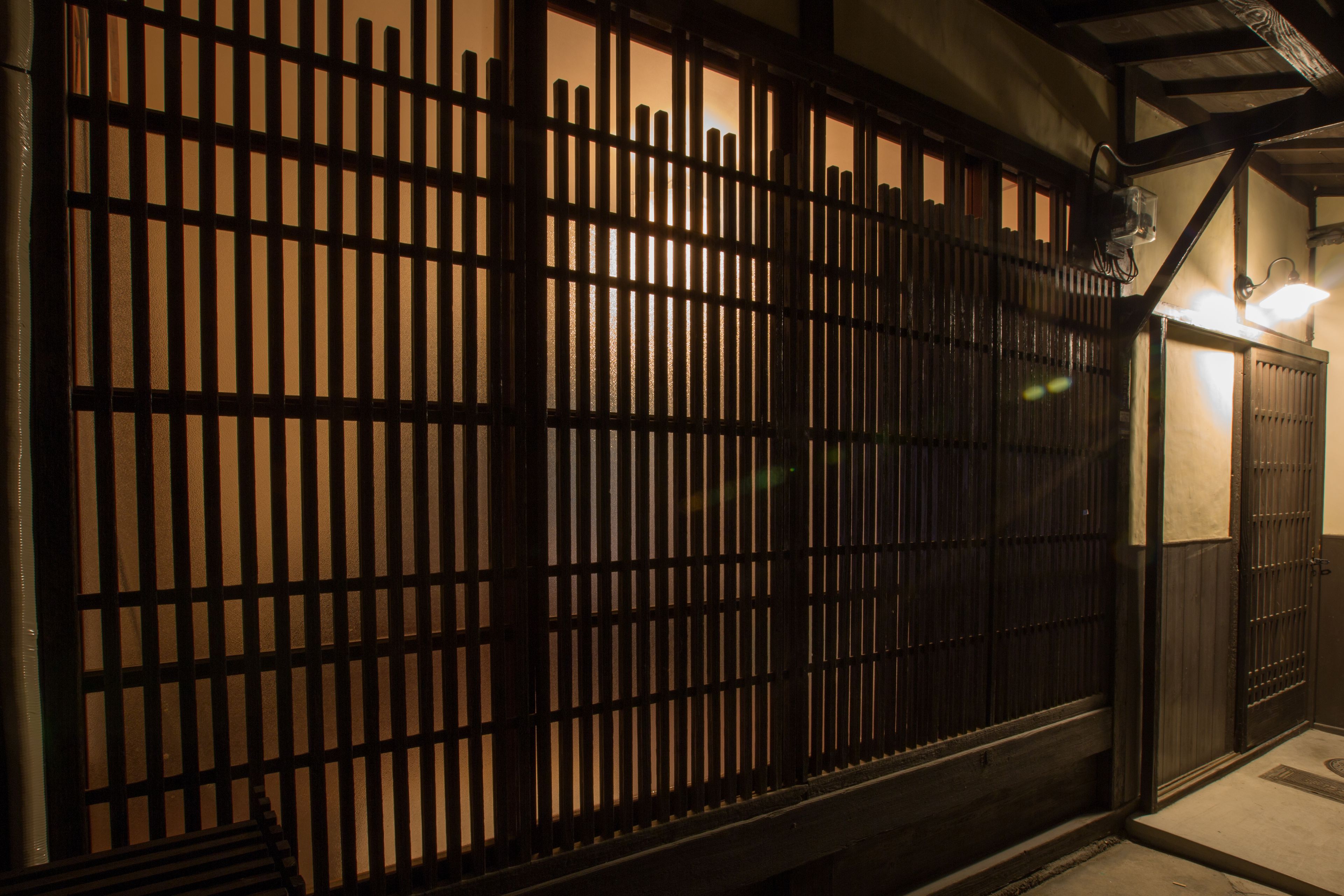A traditional Japanese-style gate with vertical wooden slats and a small lantern on the right.