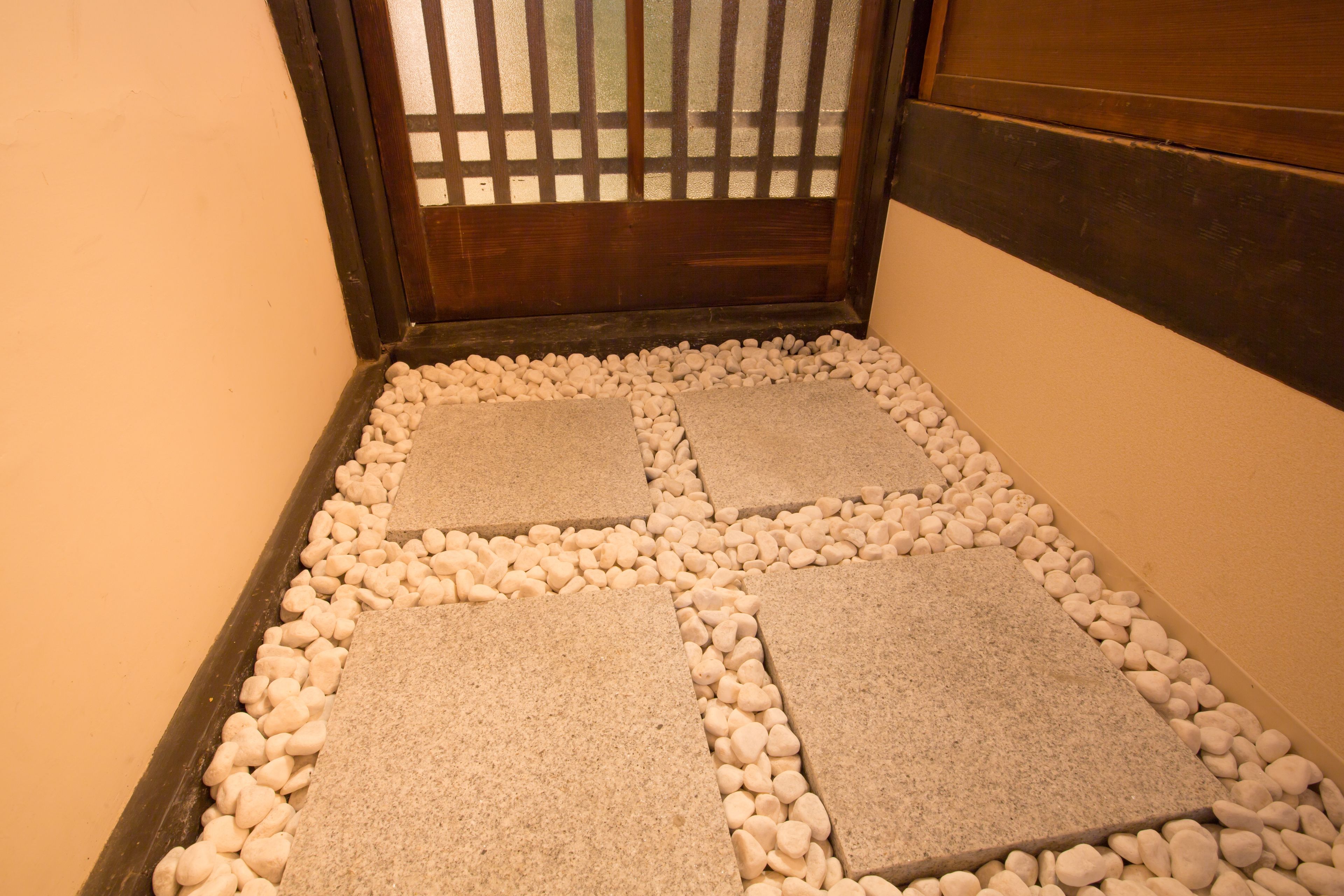 Une entrée traditionnelle japonaise avec une porte en bois, un sol recouvert de tatamis et un chemin de pierre menant à un paravent shoji.