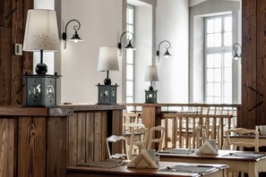 A dining area with wooden furniture, tables, and chairs, and wall-mounted lamps. - Malom Hotel és Étterem (Debrecen)