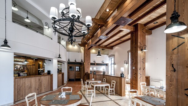 A spacious dining area with wooden beams, white tables, and chairs. A bar is visible in the background. - Malom Hotel és Étterem (Debrecen)