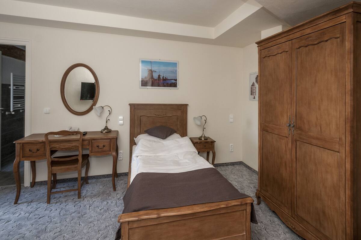 Ein Schlafzimmer mit Bett, Schreibtisch, Stuhl, Kleiderschrank, Spiegel und einem Bild an der Wand.