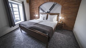 A bedroom with a brick wall, a large bed with white linens, a wooden bench, and two bedside tables with lamps. - Malom Hotel és Étterem (Debrecen)