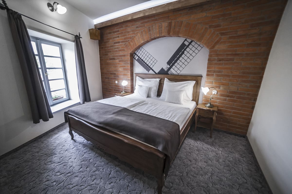 Ein Schlafzimmer mit Backsteinwand, einem großen Bett mit weißer Bettwäsche, einer Holzbank und zwei Nachttischen mit Lampen.