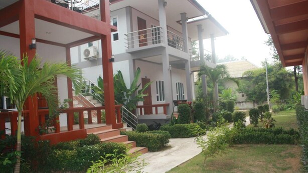 A multi-story building with a red and white exterior, a balcony on the upper floor, and a well-maintained garden with various plants and a pathway. - Tamarind Twin Resort (Ko Lanta)