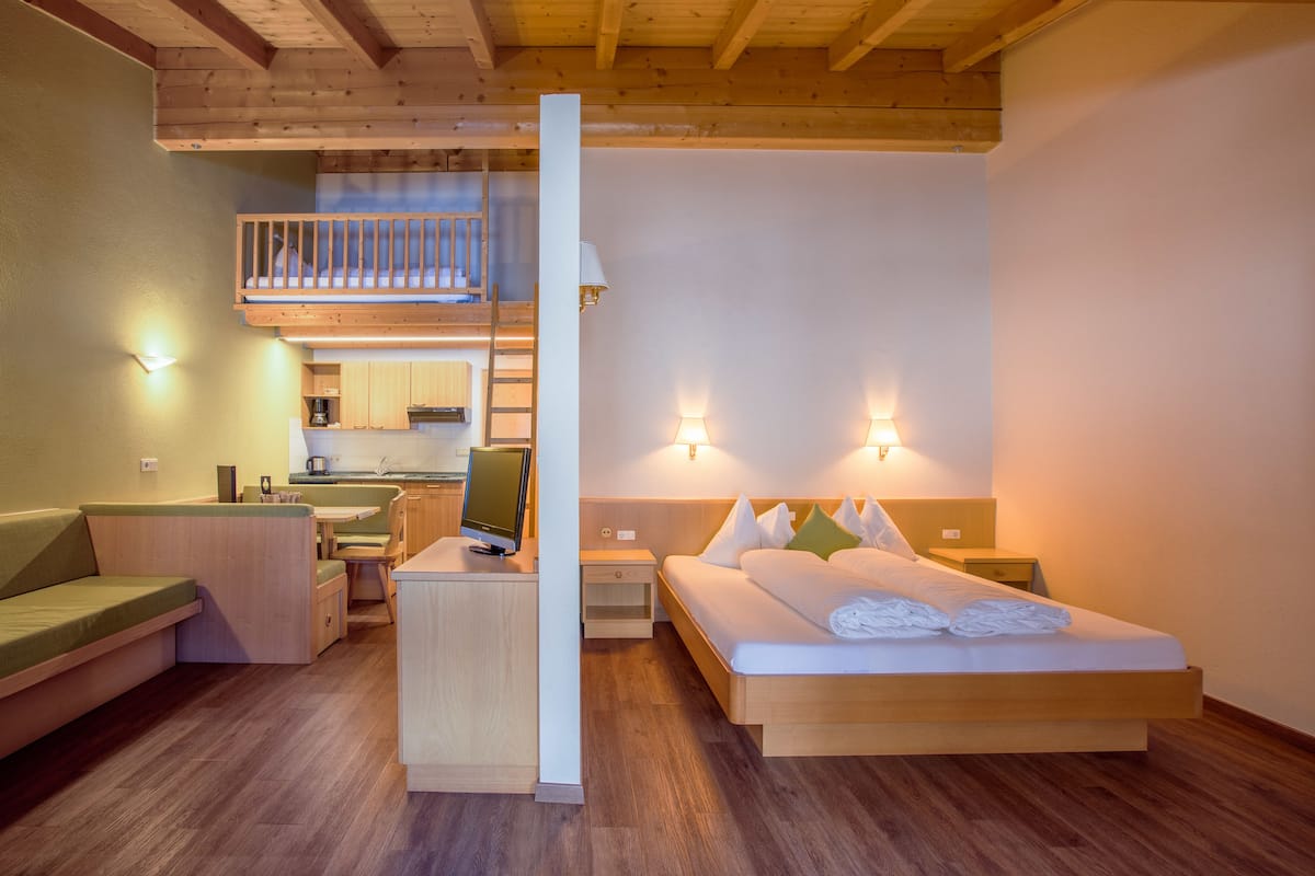 Une chambre d’hôtel moderne avec un lit en mezzanine, un bureau et une kitchenette.