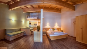 Una habitación moderna y bien iluminada con techo de madera, una cama con almohadas, un sofá, un escritorio con computadora y una pequeña cocina.