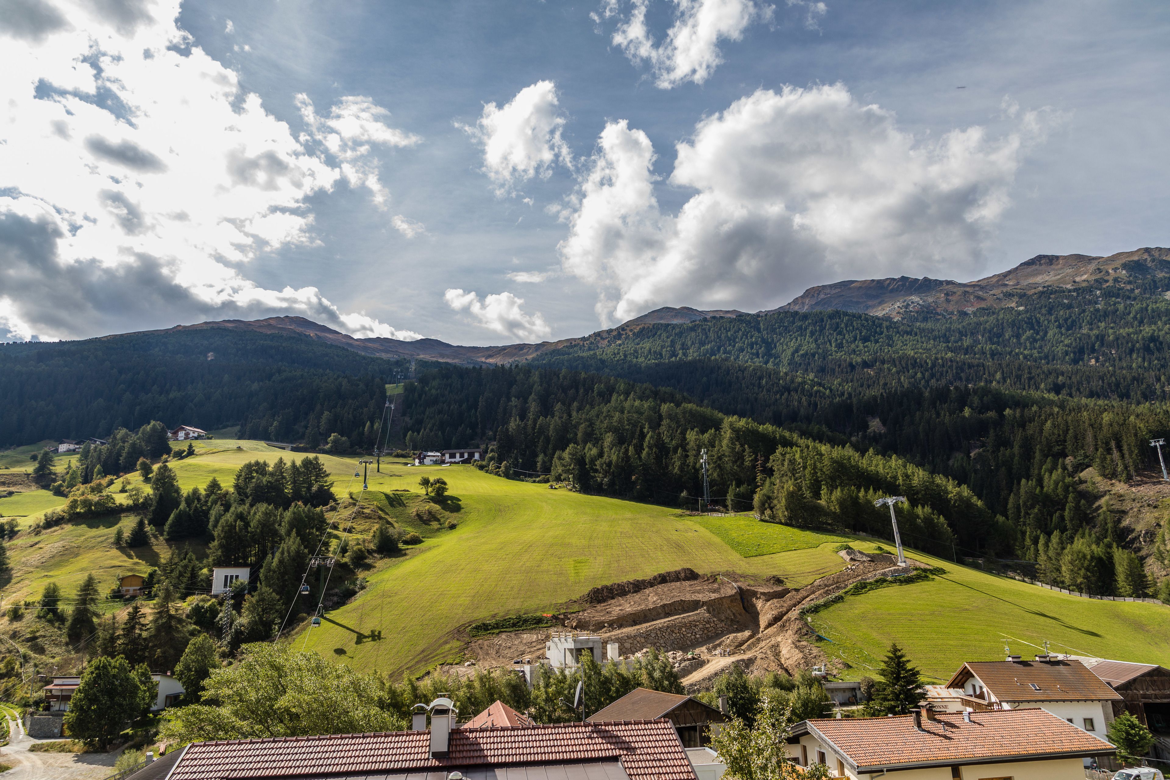 Un paysage rural avec des maisons, un champ verdoyant et des montagnes en arrière-plan.
