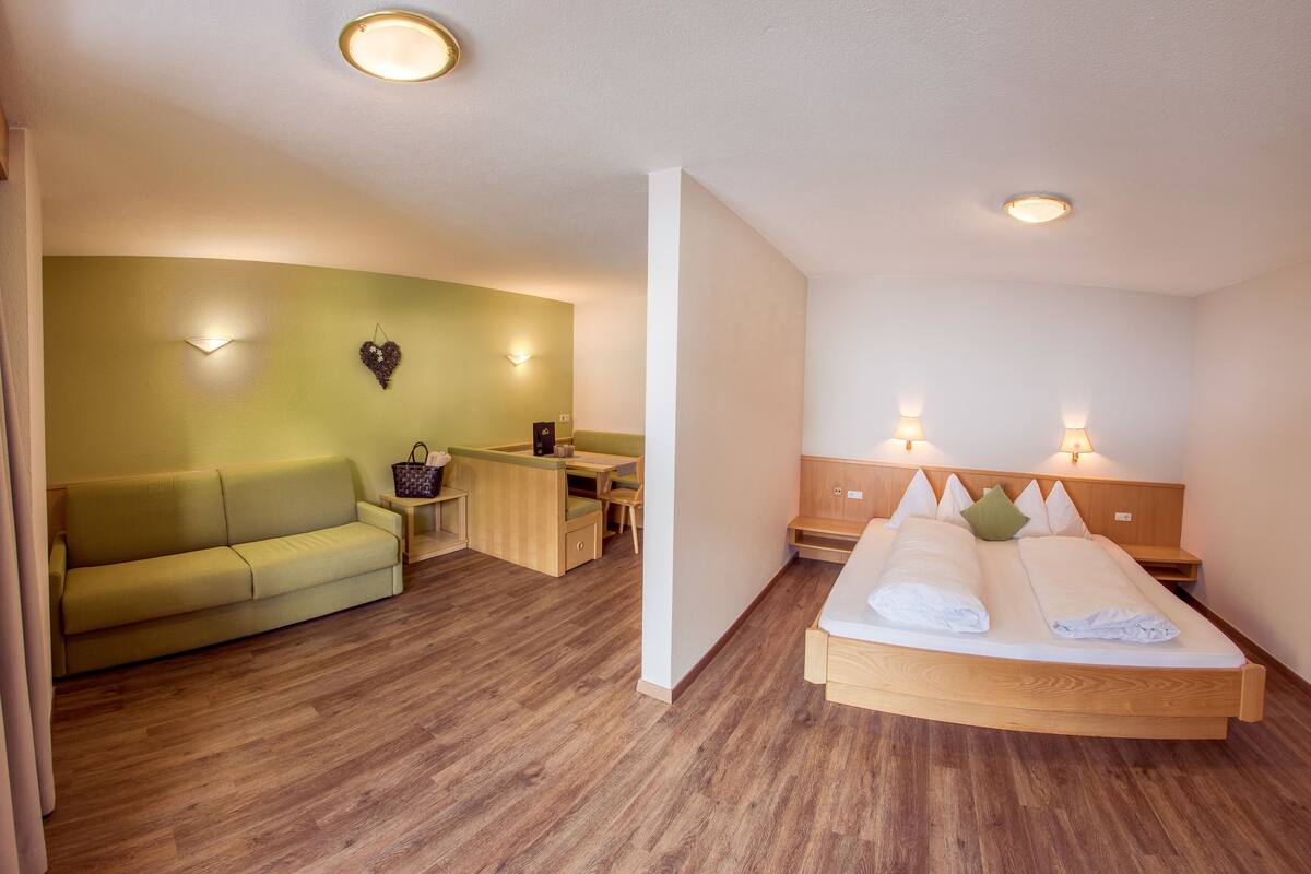 Une chambre d’hôtel avec un lit, un canapé vert, un bureau et une petite table.