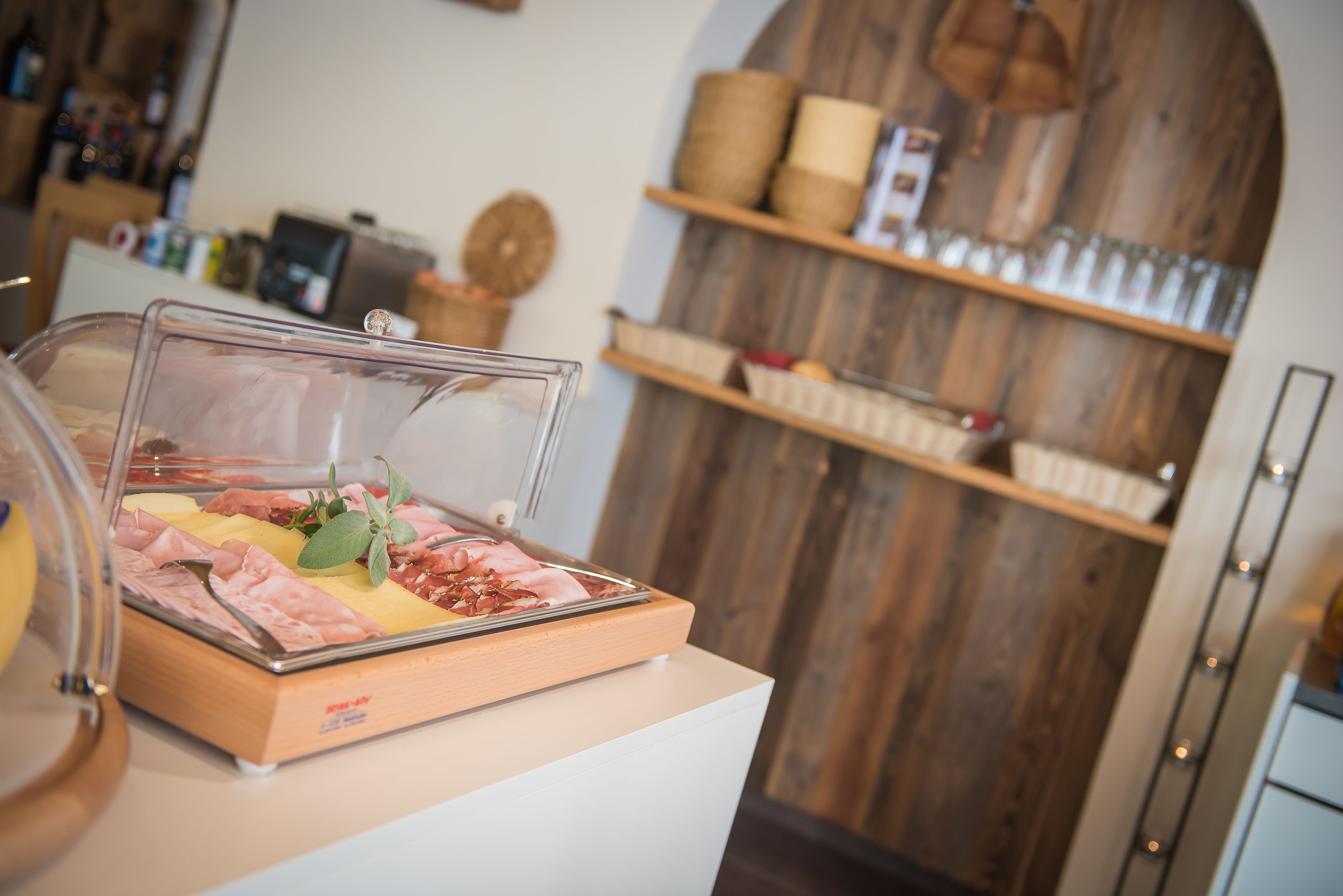 A buffet area with a variety of meats and cheeses, a wooden wall with shelves, and a counter with a cash register.