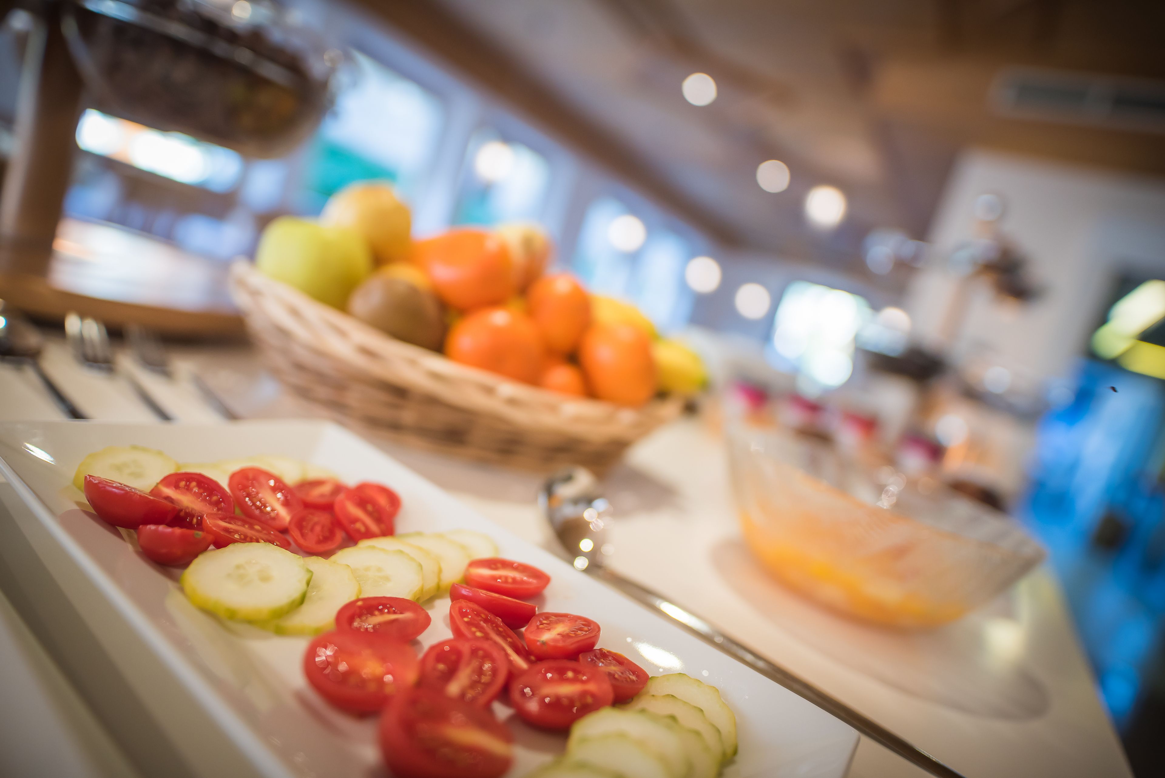 A buffet with sliced tomatoes, cucumbers, and a bowl of oranges.