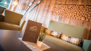 Una mesa de madera con un menú, una pequeña planta en maceta y un sofá con cojines escoceses en una habitación acogedora con paredes de madera y una ventana.