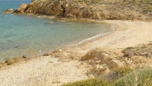 A coastal landscape with a sandy beach, rocky outcrops, and a clear view of the sea. - Kohili Studios (Paros)