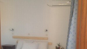 A small, neatly made bed with white linens, a wooden headboard, and a small bedside table with a lamp. - Kohili Studios (Paros)