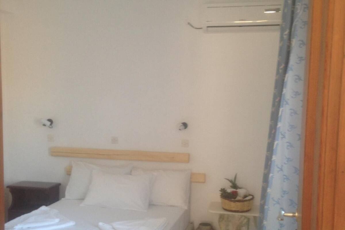 A small, neatly made bed with white linens, a wooden headboard, and a small bedside table with a lamp.