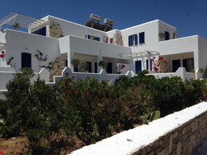 A white building with multiple balconies and a stone wall in the foreground. - Kohili Studios (Paros)
