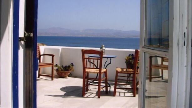 A balcony with a table and chairs, overlooking a body of water and distant mountains. - Kohili Studios (Paros)