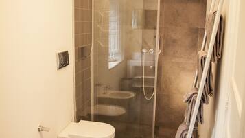 A modern bathroom with a glass-enclosed shower, a bidet, and a towel rack.