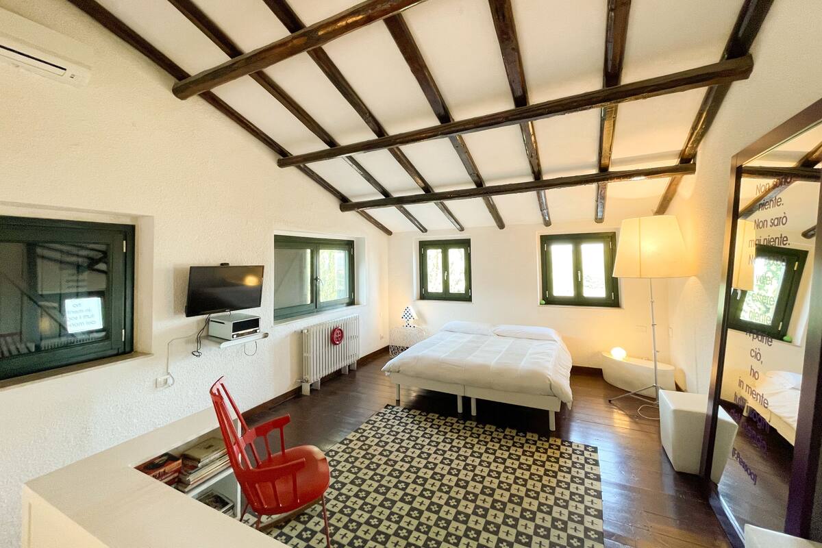 A bedroom with a bed, a TV, a red chair, and a patterned rug.
