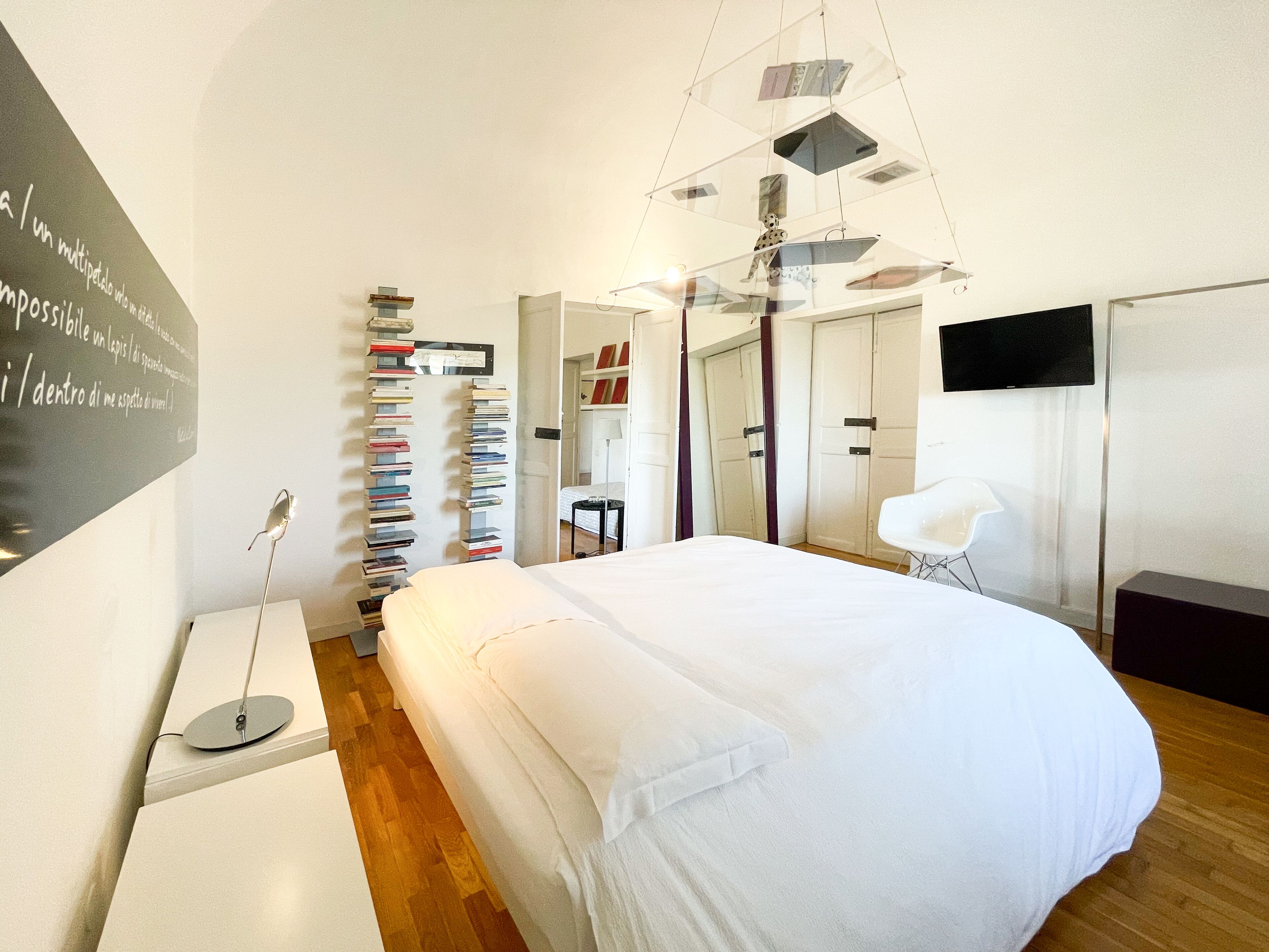 A modern bedroom with a large bed, a bookshelf, a desk, and a TV.