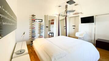 A modern bedroom with a large bed, a bookshelf, a desk, and a TV.