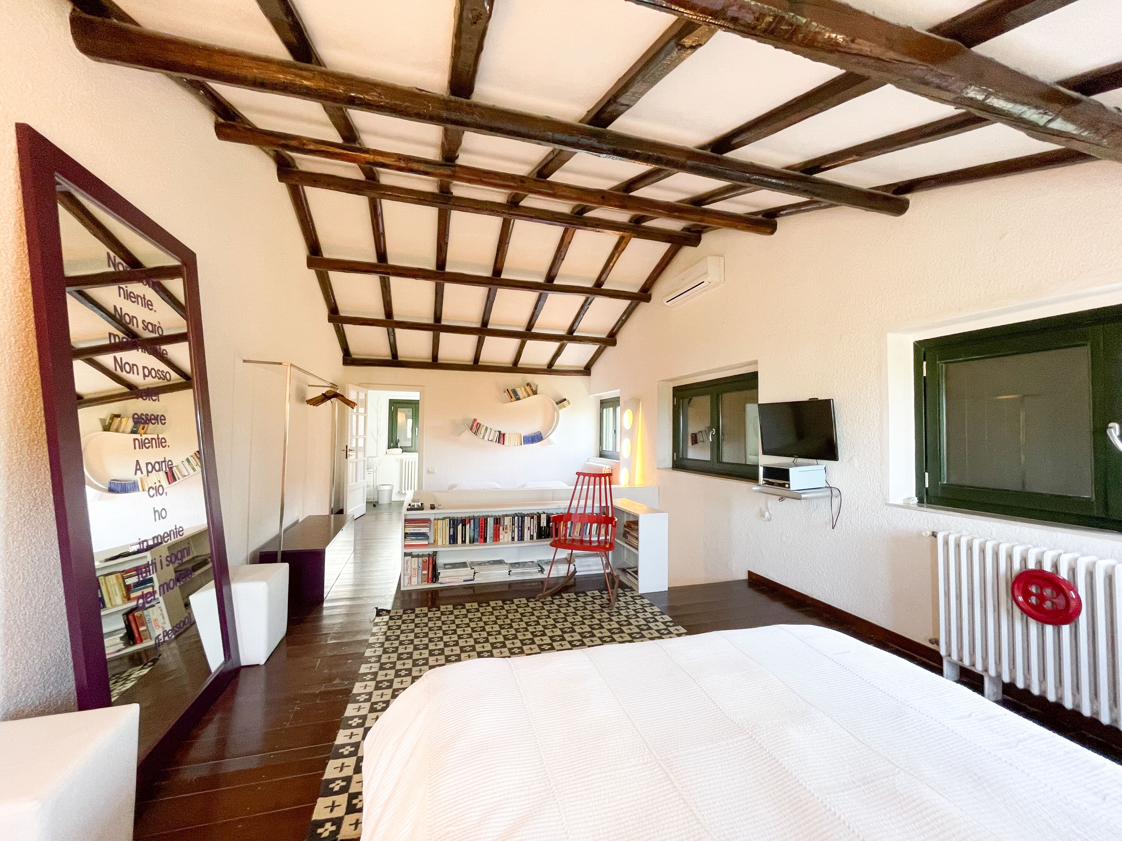 Un dormitorio con techo de madera, una cama, un televisor, un radiador y una estantería.