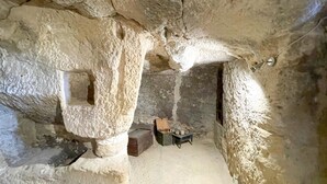 Un interior que recuerda a una cueva, con paredes de piedra tosca, una mesa pequeña con una caja y una botella en el suelo.