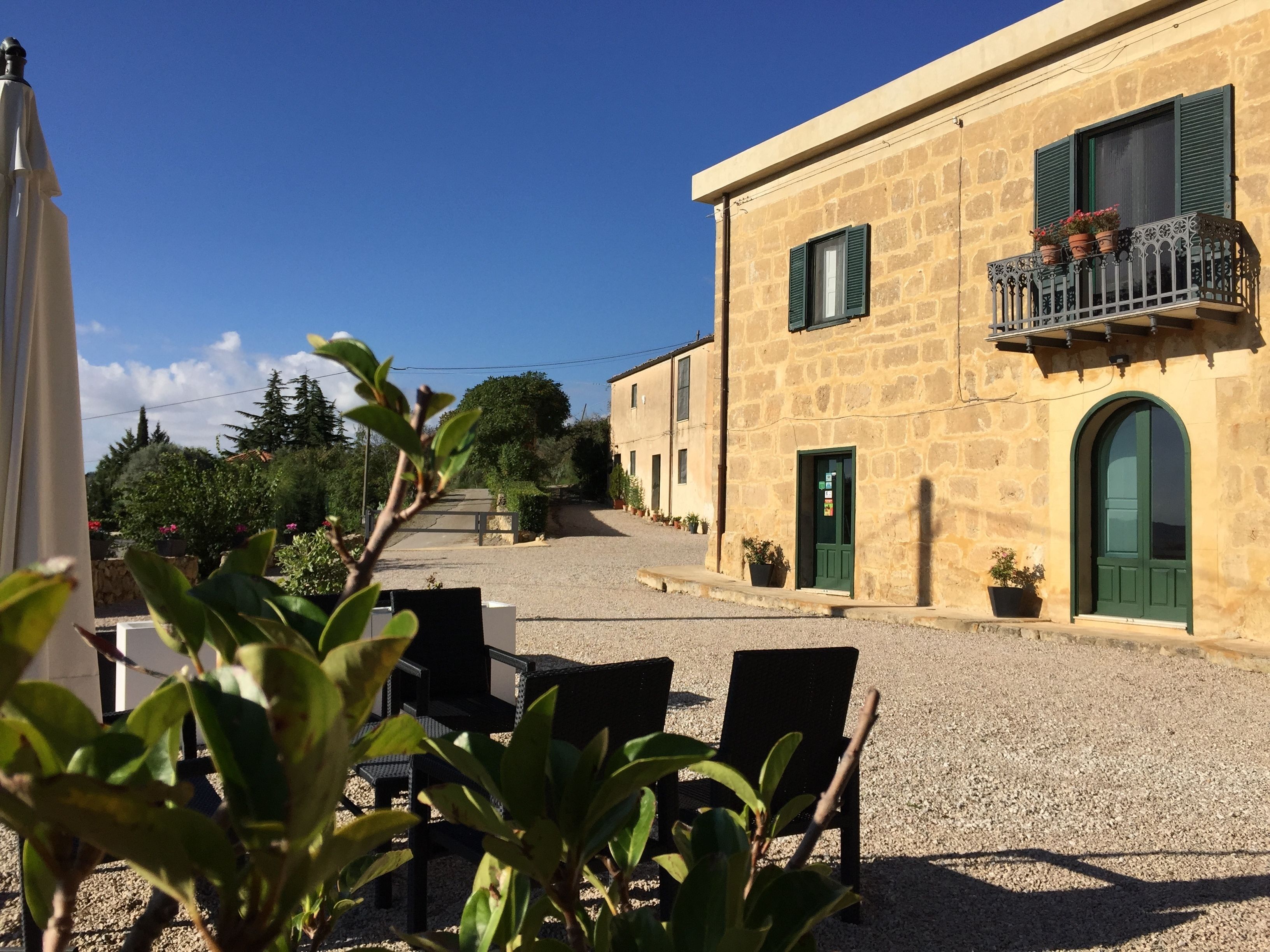 A courtyard with outdoor seating, a stone building with a balcony, and a clear blue sky.