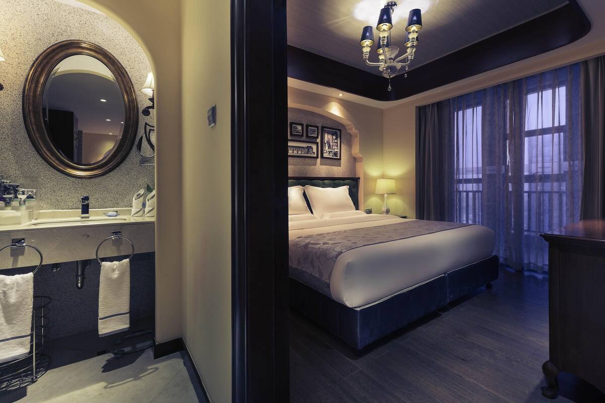 Una habitación de hotel con una cama grande, un tocador con espejo y una araña.