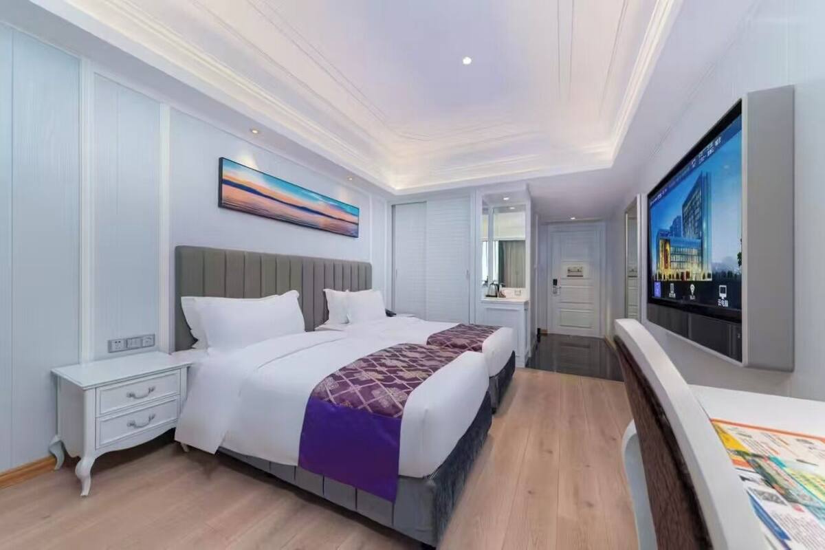 Una habitación de hotel con una cama grande, un televisor, un cuadro y un espejo.