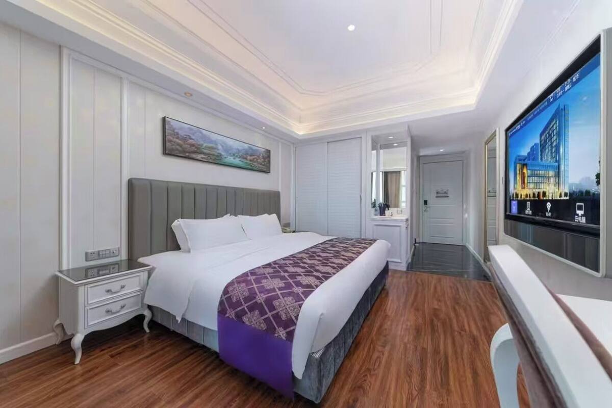 Una habitación de hotel con cama, mesita de noche, televisor y un ventanal grande.