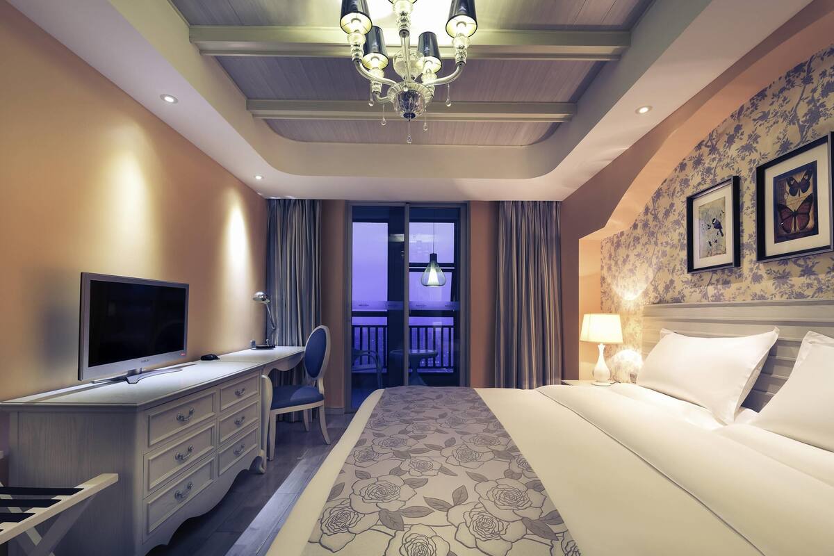 Habitación de hotel con cama, escritorio, silla, televisión y vistas al balcón.