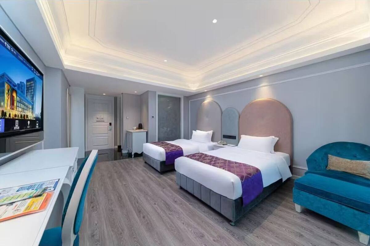 Una habitación de hotel con dos camas, un escritorio, un televisor y un sofá azul.