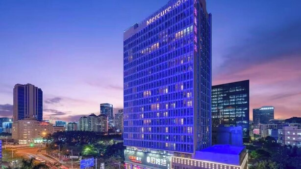 Ein Hochhaus-Hotel mit auffälliger Beschilderung, umgeben von anderen Gebäuden und einer belebten Straße bei Einbruch der Dunkelheit.