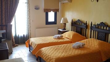 Ein Hotelzimmer mit zwei Betten, einem Heizkörper, einem Fenster mit Vorhängen, einer Lampe und einer Wandklimaanlage.