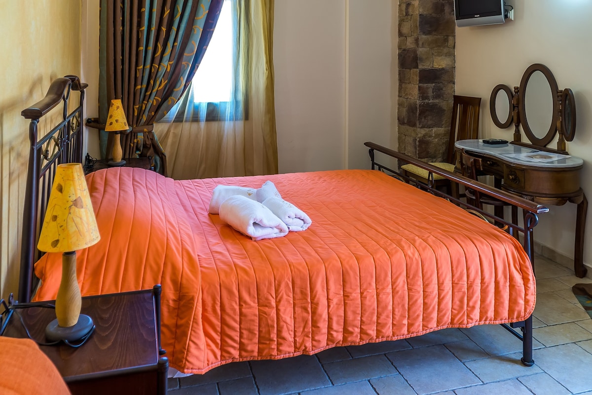 A neatly made bed with a quilt, a bedside lamp, a wooden nightstand, a dresser with a mirror, and a television mounted on the wall.