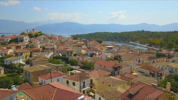 A coastal town with terracotta-roofed buildings, a visible harbor, and mountains in the background.