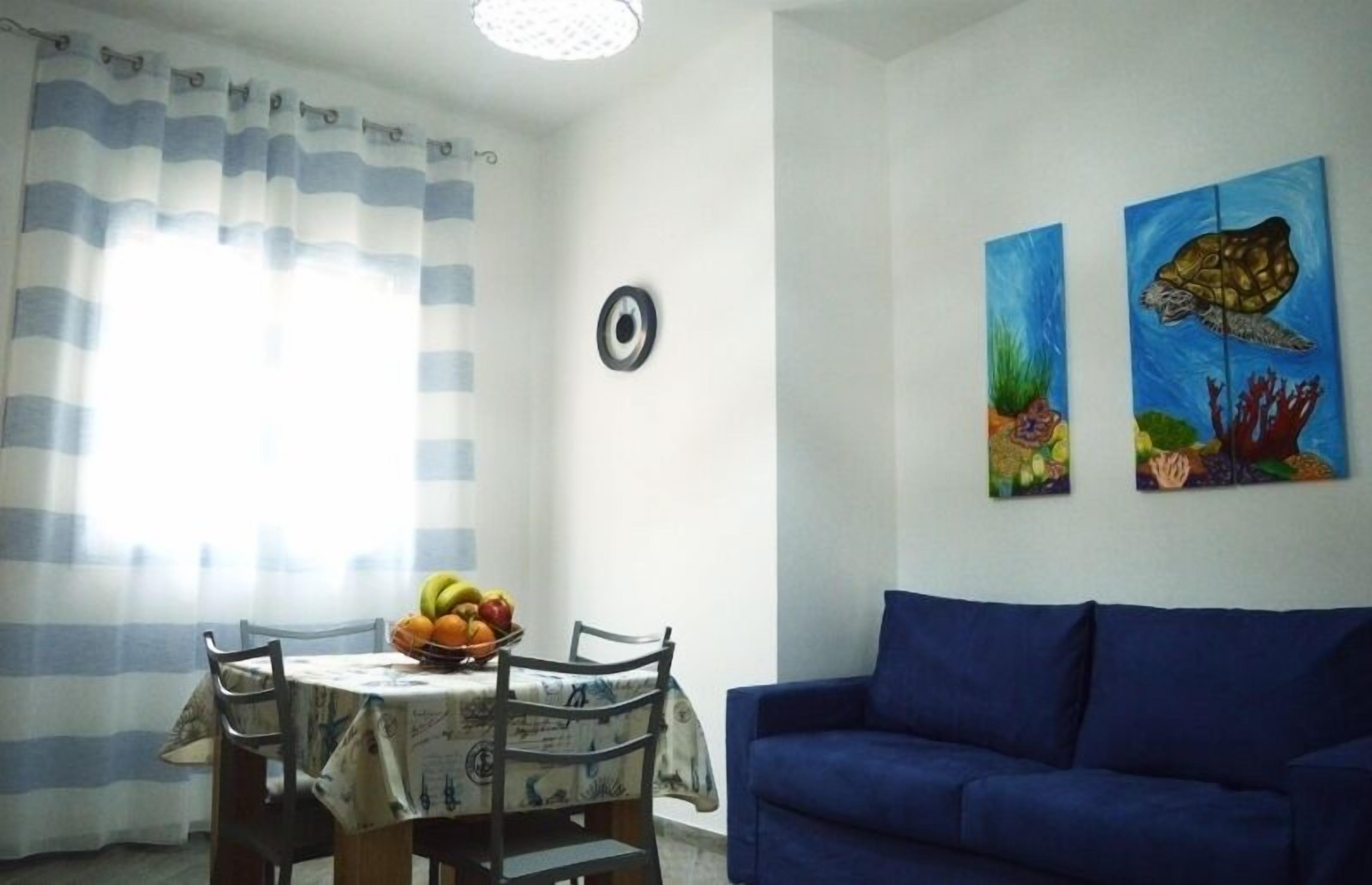 Ein Essbereich mit einem für zwei Personen gedecktem Tisch, einem blauen Sofa und zwei Bildern von Meeresschildkröten an der Wand.
