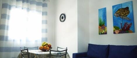 Ein Essbereich mit einem für zwei Personen gedecktem Tisch, einem blauen Sofa und zwei Bildern von Meeresschildkröten an der Wand.