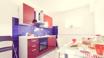 Una cocina moderna con armarios rojos y blancos, un salpicadero de azulejos azules y un comedor con mesa y sillas de vidrio.