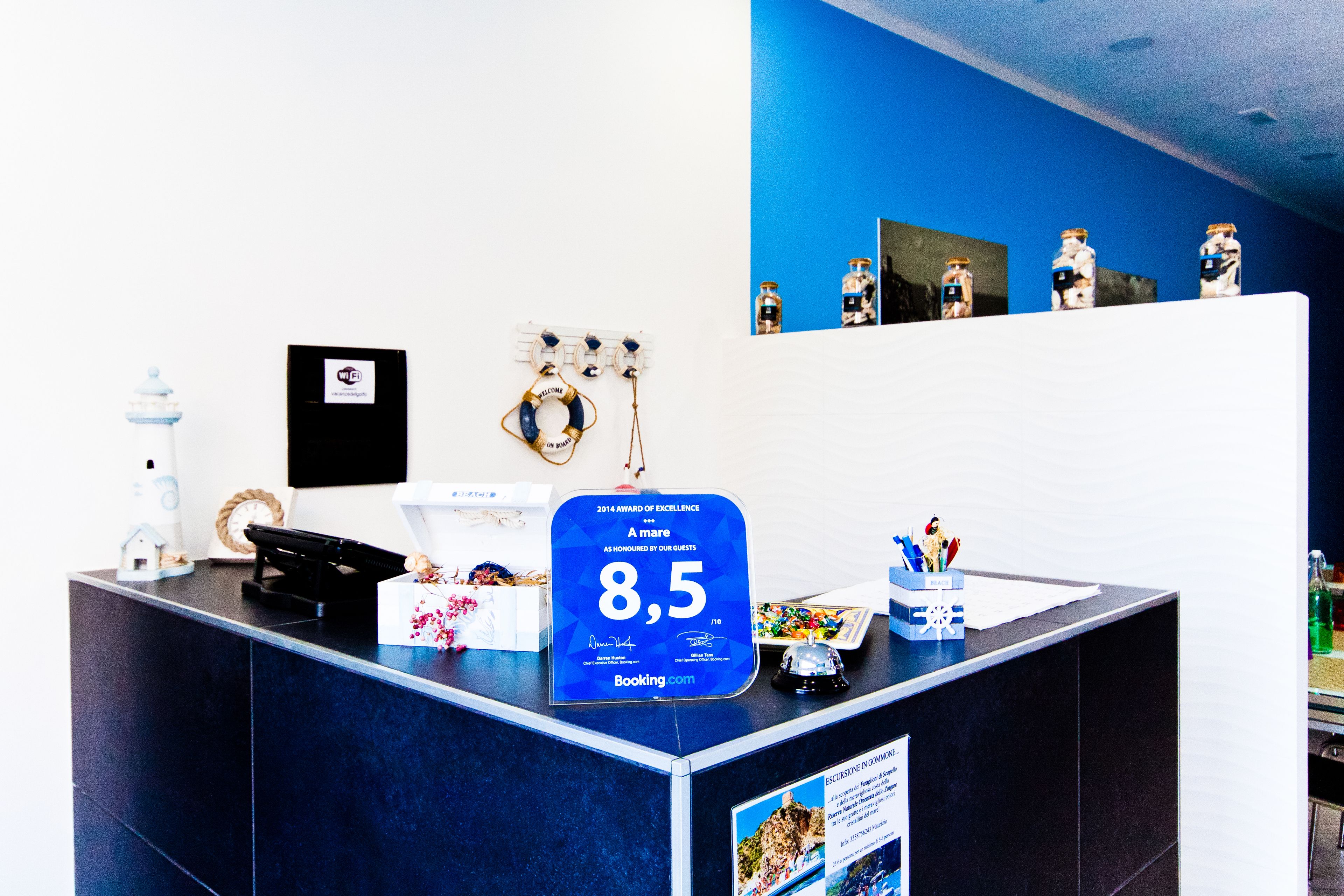 A reception desk with a blue sign indicating an 8.5 rating, a clock, a small house decoration, and a water dispenser.