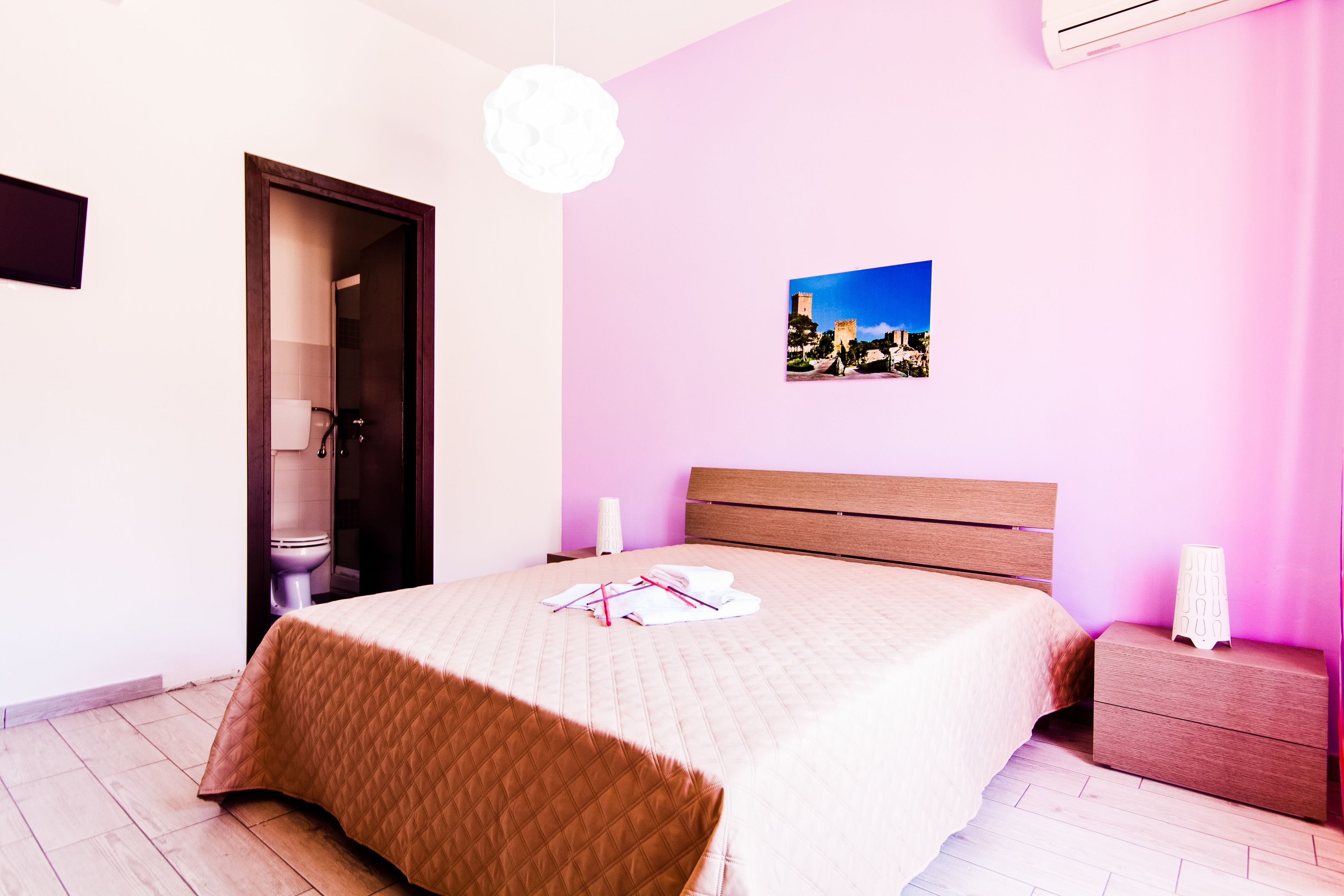A bedroom with a bed, a bedside table, a nightstand, a picture on the wall, and a door leading to a bathroom.