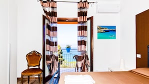 Ein Schlafzimmer mit Bett, Stuhl und Blick auf einen Balkon mit Vorhängen.