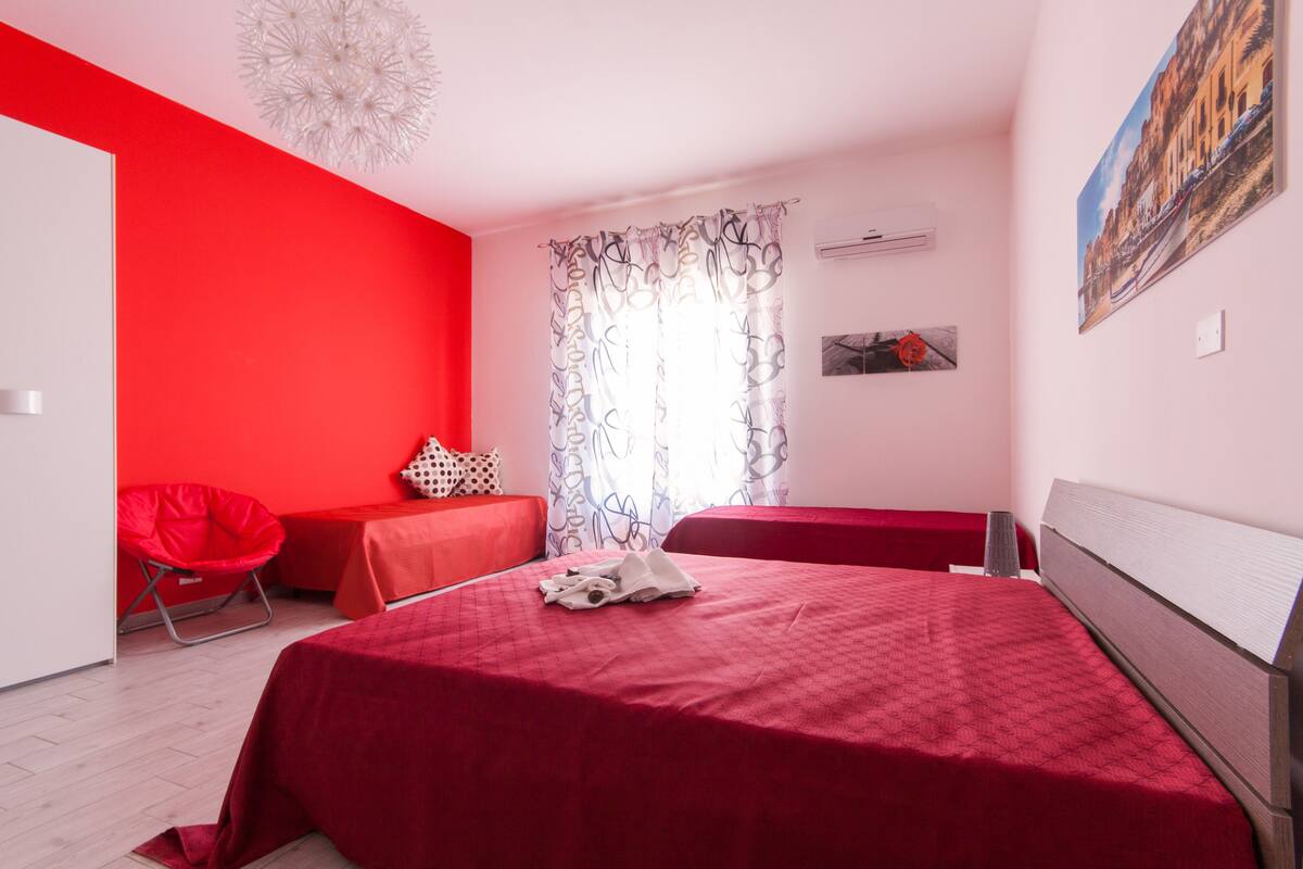 Een slaapkamer met een rood beddegoed, een rode stoel en een witte plafondlamp.