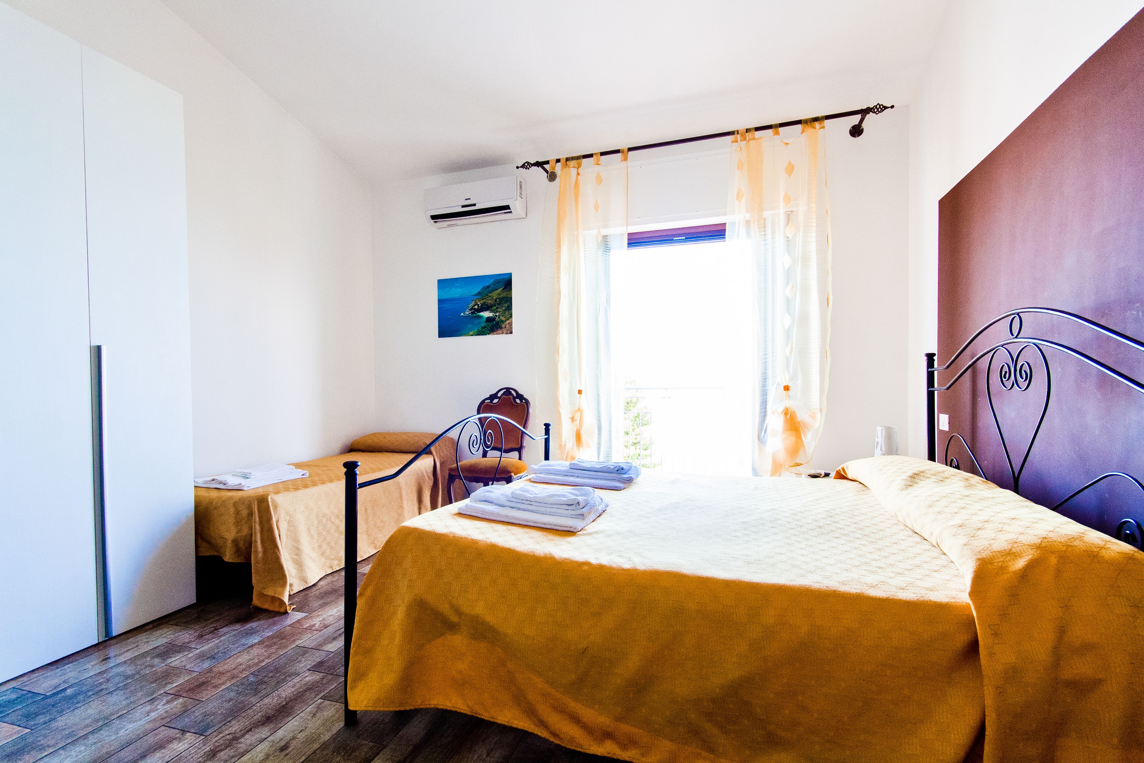 A bedroom with a bed, a chair, a table, and a window with curtains.