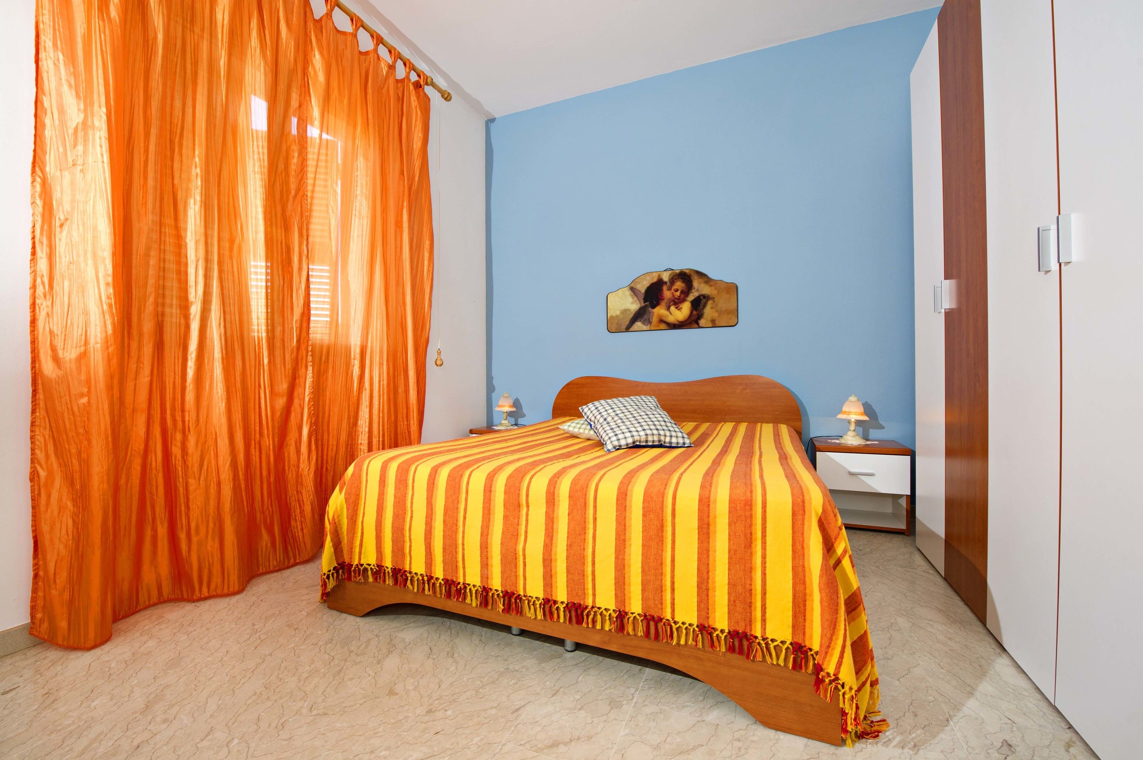 Une chambre à coucher avec un lit, des rideaux orange, un mur bleu, une table de chevet et une lampe.