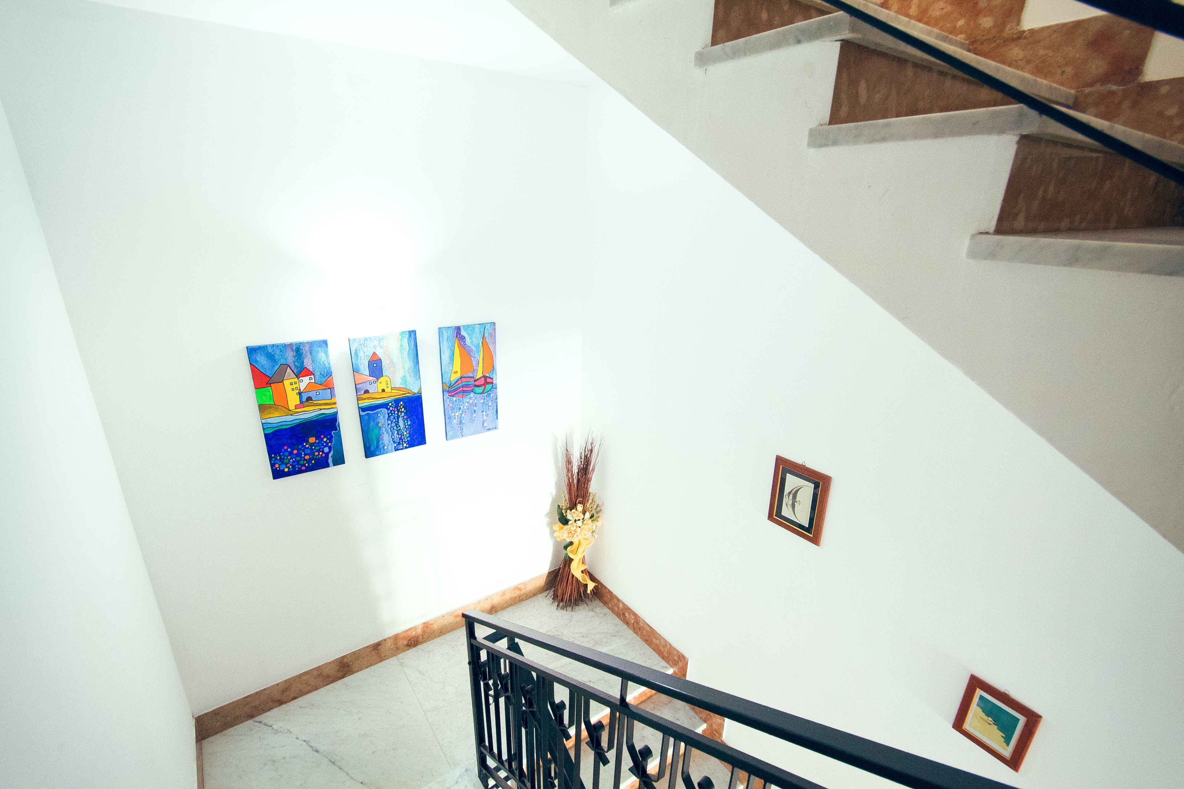 A staircase with a handrail, a wall with three framed artworks, and a small framed picture.