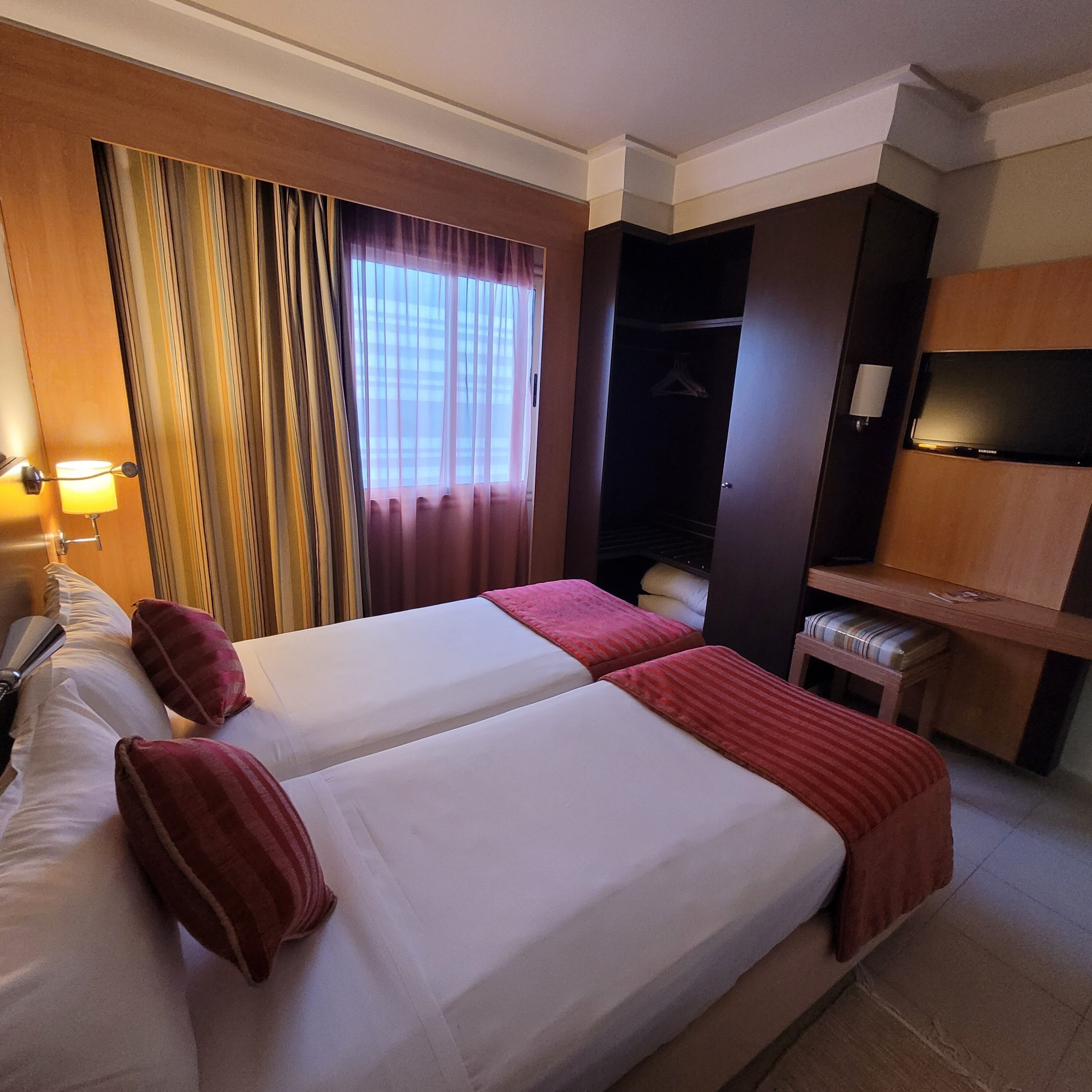 A hotel room with two beds, a desk, a TV, and a wardrobe.