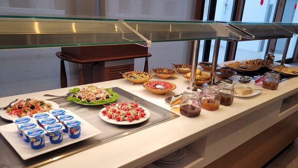 Ein reichhaltiges Buffet mit verschiedenen Speisen und Getränken, darunter Salate, Früchte und Joghurts.